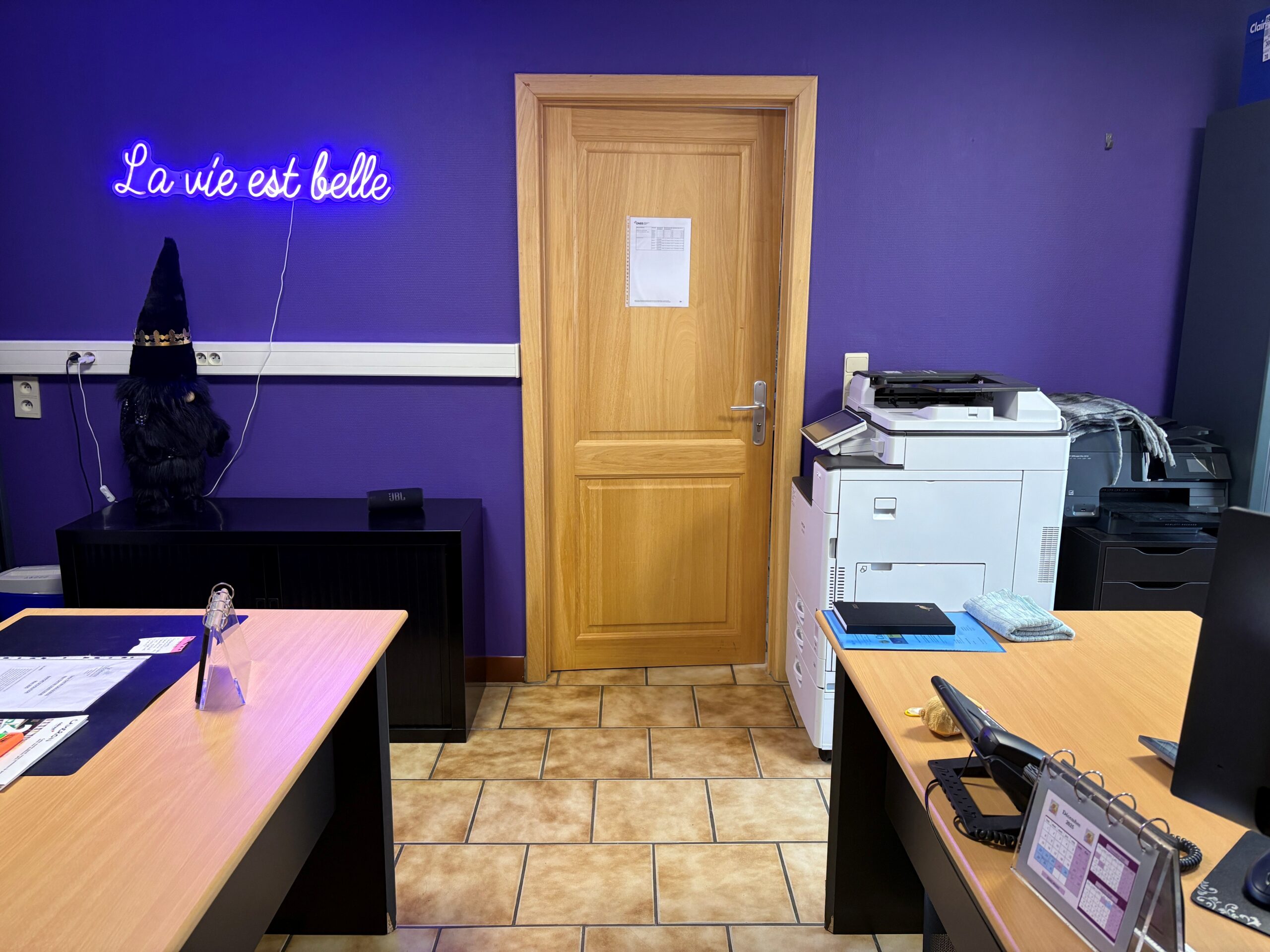 Le bureau du personnel de la maison Ewdelweiss composé avec deux bureau, des murs mauves et une enseigne "la vie est belle" également mauve et lumineuse